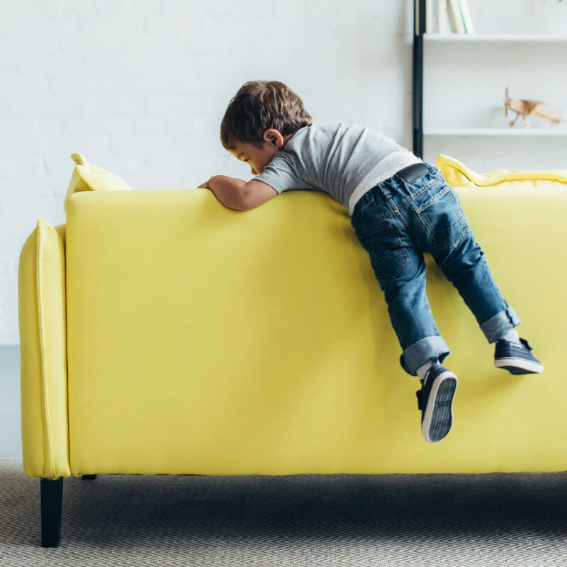 Child climbing on the back of a yellow couch.