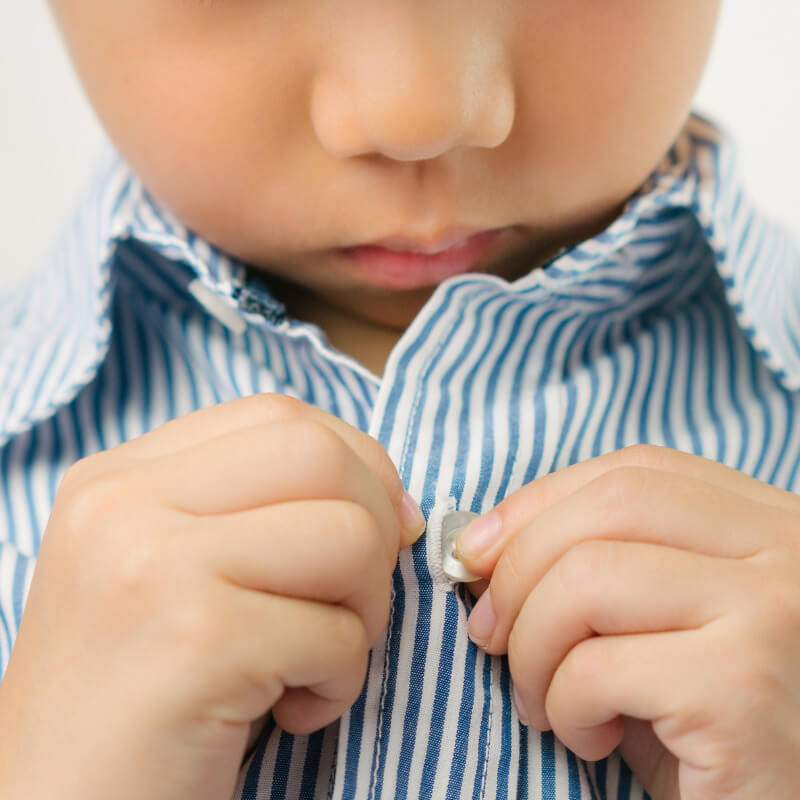 Child's hands buttoning a shirt, showing hand strength during a functional activity.