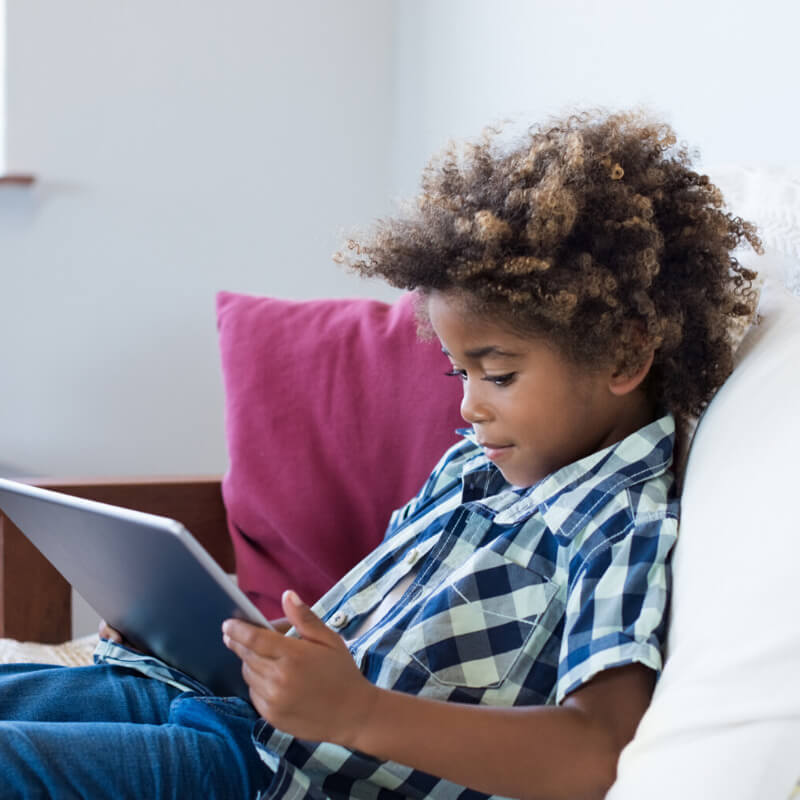 kid sitting on couch looking at tablet
